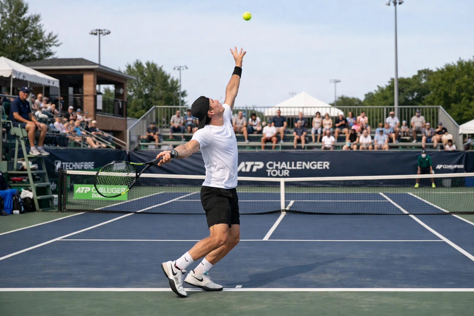 Campo da tennis Challenger con giocatore emergente in azione, piccolo stadio con pochi spettatori, atmosfera intima